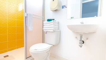 A bathroom with a yellow-tiled shower, a white toilet, a sink, and a towel rack with folded towels.