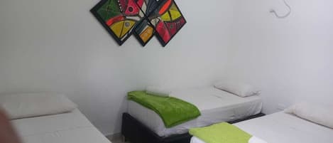 A room with three beds, each with a white mattress and a green blanket. There is a wall-mounted air conditioner and a colorful abstract artwork above the beds.