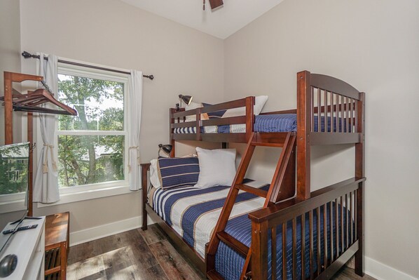 A bunk bed with a wooden frame and blue bedding, a desk with a chair, and a window with curtains. - Lake Norman - Tranquility Cove - Beautiful Lakefront Apartment (Mooresville)