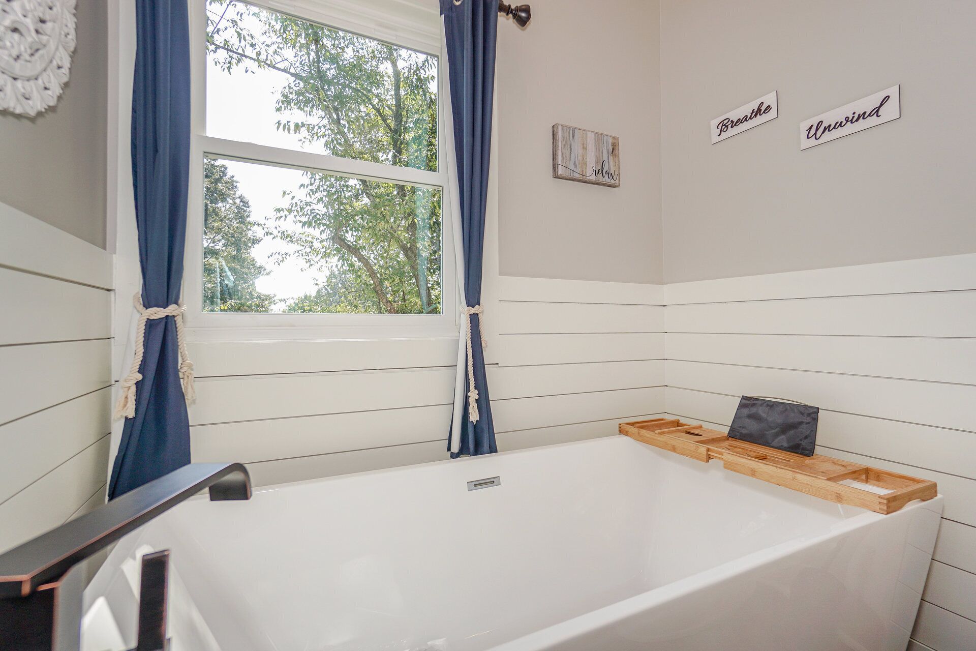 Une salle de bain avec une baignoire, une fenêtre avec des rideaux et des panneaux indicateurs fixés au mur.