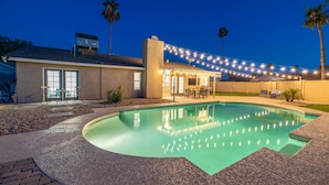 A swimming pool with a stone deck, a covered patio area with outdoor furniture, and string lights. - Scottsdale's Best: Sun, Swing & Gourmet Eats! (Scottsdale)