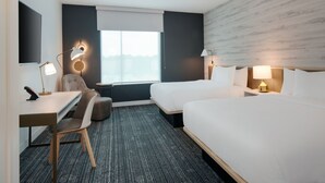 Hotellihuone, jossa on työpöytä, kaksi sänkyä, tuoli ja ikkuna, josta on näkymä.