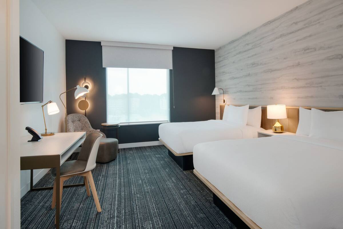 Habitación de hotel con escritorio, dos camas, una silla y ventana con vistas.