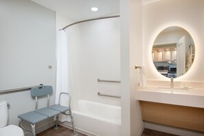 Een moderne badkamer met een douche, toilet, wastafel met spiegel, en een rolstoel toegankelijke bank.