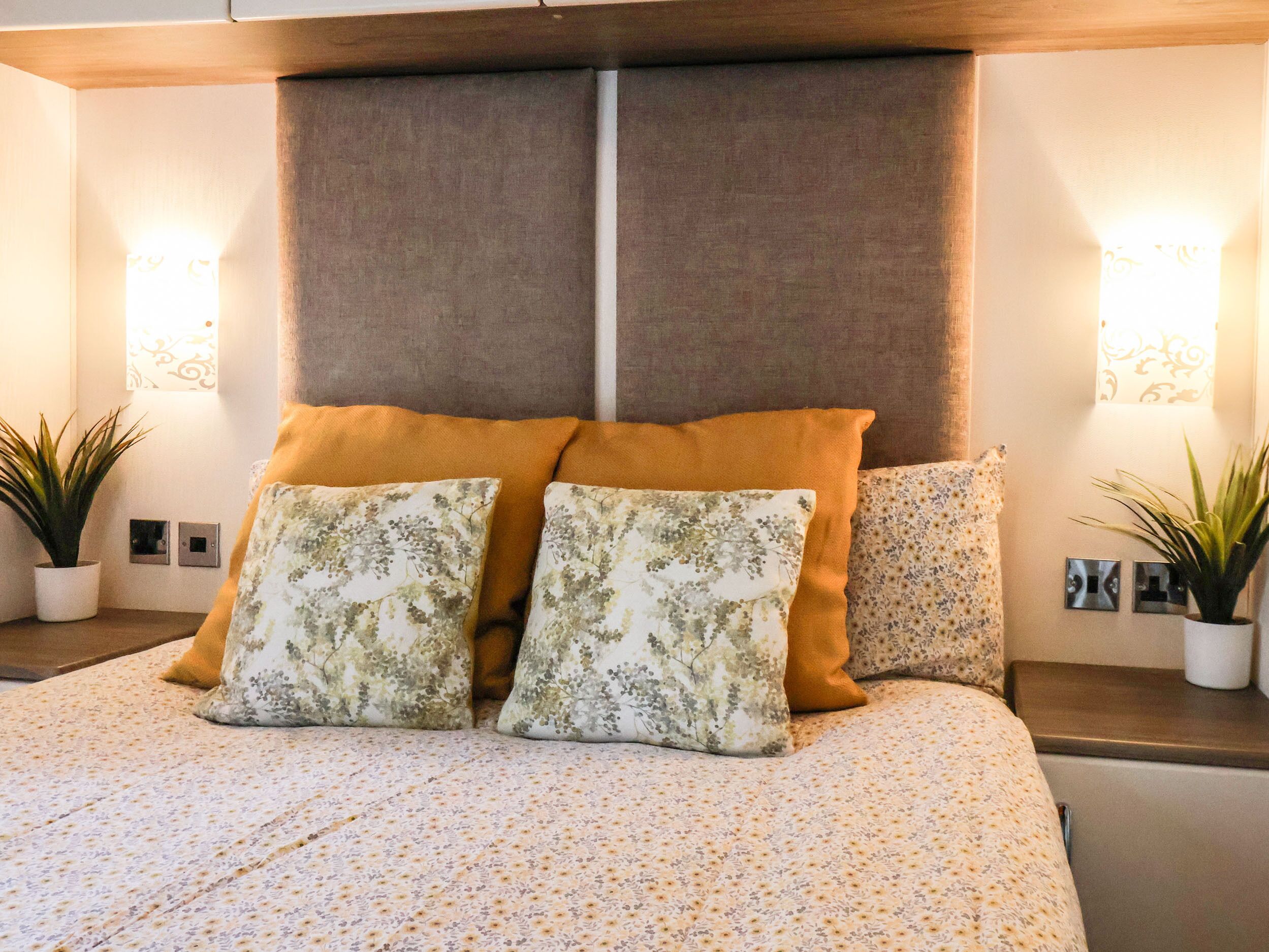 Un dormitorio con una cama, dos mesitas de noche, dos lámparas de pared y dos plantas en macetas.