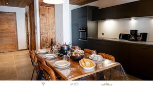 A modern kitchen with dark cabinets, a wooden dining table set for a meal, and a large pendant light.