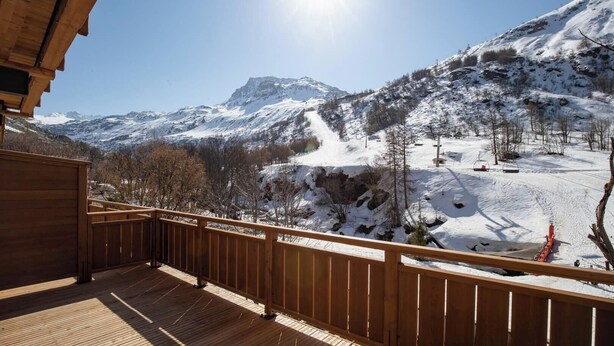 A wooden deck with a view of snow-covered mountains and a ski lift in the background.