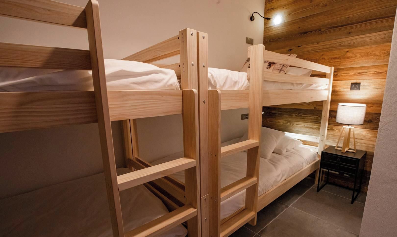 Une chambre avec un lit superposé doté d’une tête de lit en bois, une table de chevet avec une lampe et un luminaire fixé au mur.