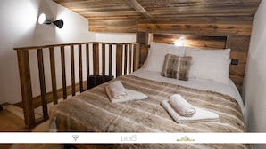 A bedroom with a wooden headboard, a bed with a striped blanket, two rolled towels, and a wall-mounted light fixture. - Marmotte 204 - Le vallonnet - New apartment up to 10 guests (BONNEVAL SUR ARC)