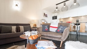 A modern living room with a sofa, coffee table, and a dining area with chairs and a kitchen in the background. - Marmotte 204 - Le vallonnet - New apartment up to 10 guests (BONNEVAL SUR ARC)