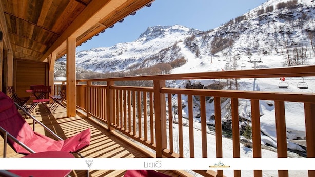 A wooden deck with chairs and tables, overlooking a snowy mountain landscape with ski lifts. - Marmotte 204 - Le vallonnet - New apartment up to 10 guests (BONNEVAL SUR ARC)