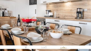 A modern kitchen with white cabinets, a wooden countertop, and a dining area set with white plates, bowls, and glasses. - Marmotte 204 - Le vallonnet - New apartment up to 10 guests (BONNEVAL SUR ARC)