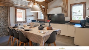 Une cuisine chaleureuse avec un coin repas, des murs en pierre, des poutres en bois et une grande fenêtre.