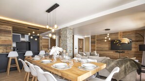 A modern dining area with a wooden table set for six, white chairs, and a stone accent wall. - Marmotte 103 - New apartment up to 10 guests with stunning view (BONNEVAL SUR ARC)