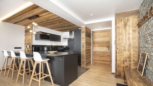 A modern kitchen with a central island, bar stools, a microwave, and a stone accent wall. - Marmotte 103 - New apartment up to 10 guests with stunning view (BONNEVAL SUR ARC)