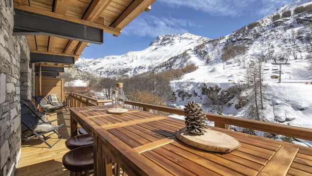 A wooden deck with a table and chairs, overlooking a snowy mountain landscape with ski slopes. - Marmotte 103 - New apartment up to 10 guests with stunning view (BONNEVAL SUR ARC)