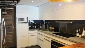 Une cuisine moderne avec des meubles blancs, un plan de travail noir, des appareils en acier inoxydable et un luminaire suspendu.
