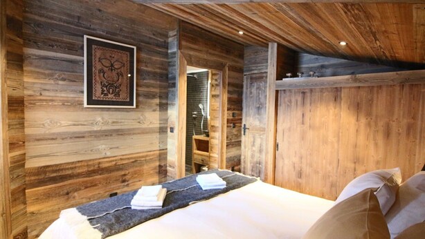 Une pièce aménagée comme un chalet en bois, avec un lit, un tableau encadré au mur et une petite étagère en bois.