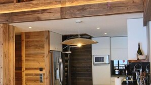 Une cuisine moderne avec des éléments en bois, un îlot central doté de tabourets et un réfrigérateur visible.