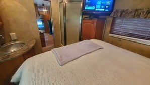 Een hotelkamer met een bed, een aan de muur bevestigde televisie, een wastafel en een raam met zonwering.