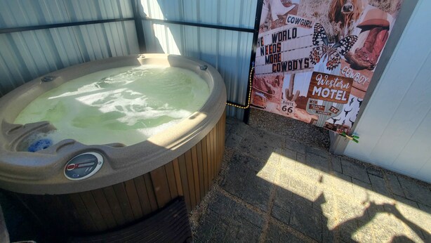 Een hottub onder een metalen dak, omringd door een golfplaten hek, met een poster die een motel met een western thema promoot.