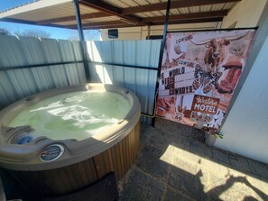 A hot tub under a metal roof, surrounded by a corrugated metal fence, with a poster advertising a Western-themed motel. - Hilton's Hometown Tower-view Hot-tub Retreat (Cisco)