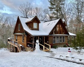 A wooden cabin with a porch, a staircase, and a snowman decoration.