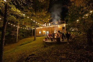Een houten gebouw met een terras, omgeven door bomen en lichtslingers.