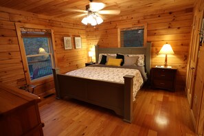 A wooden-paneled bedroom with a bed, nightstands, and a ceiling fan.
