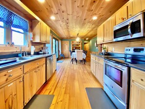Interieur van een houten chalet met een keuken, eethoek en een zichtbare deur naar een andere kamer.