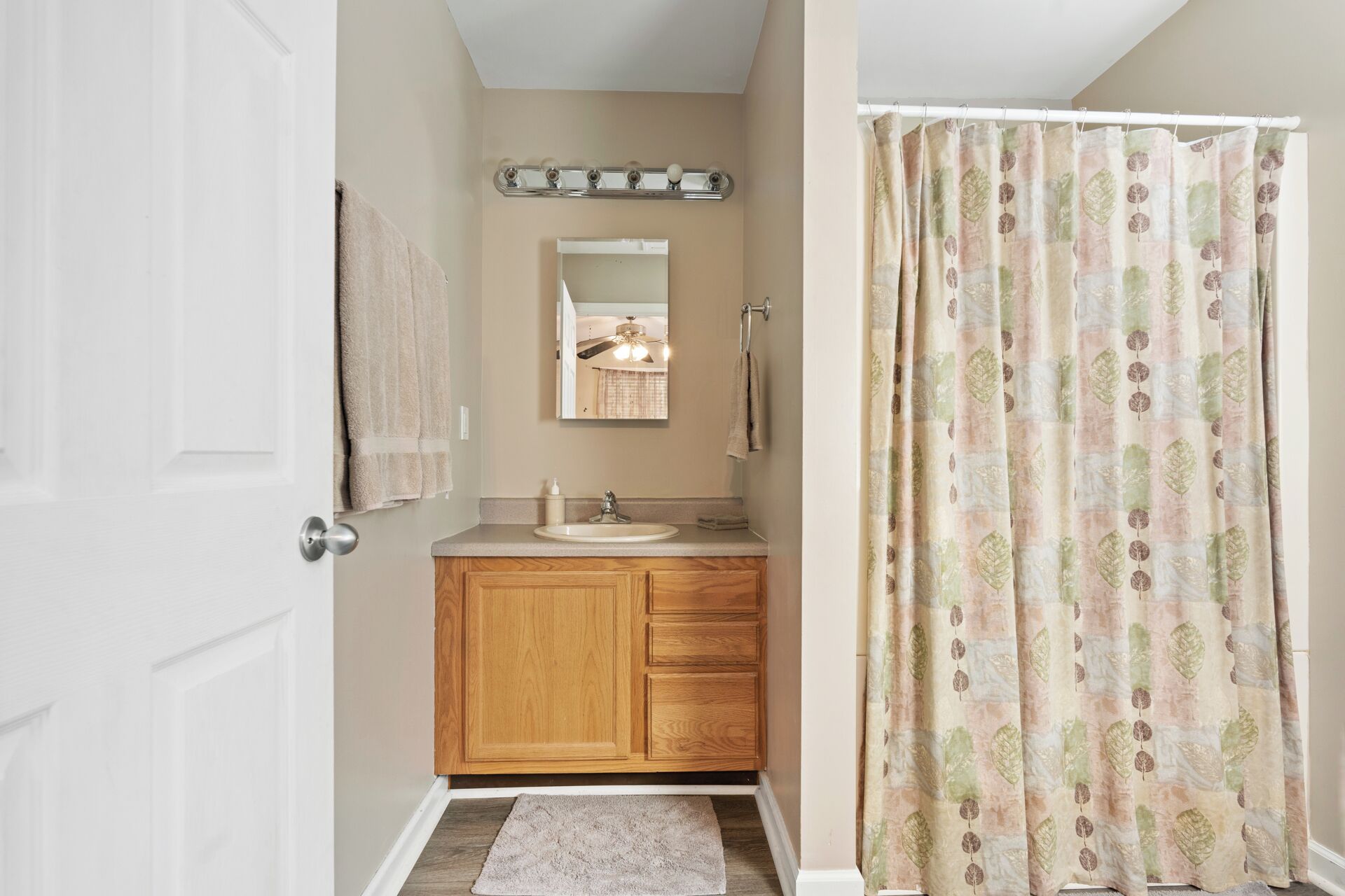 A bathroom with a wooden vanity, a sink, a mirror, and a shower curtain with a leaf pattern.