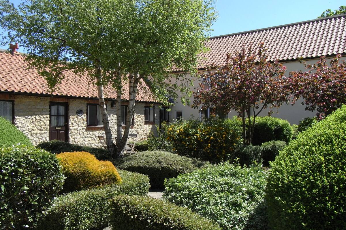 A stone building with a tiled roof, surrounded by well-maintained hedges and trees.