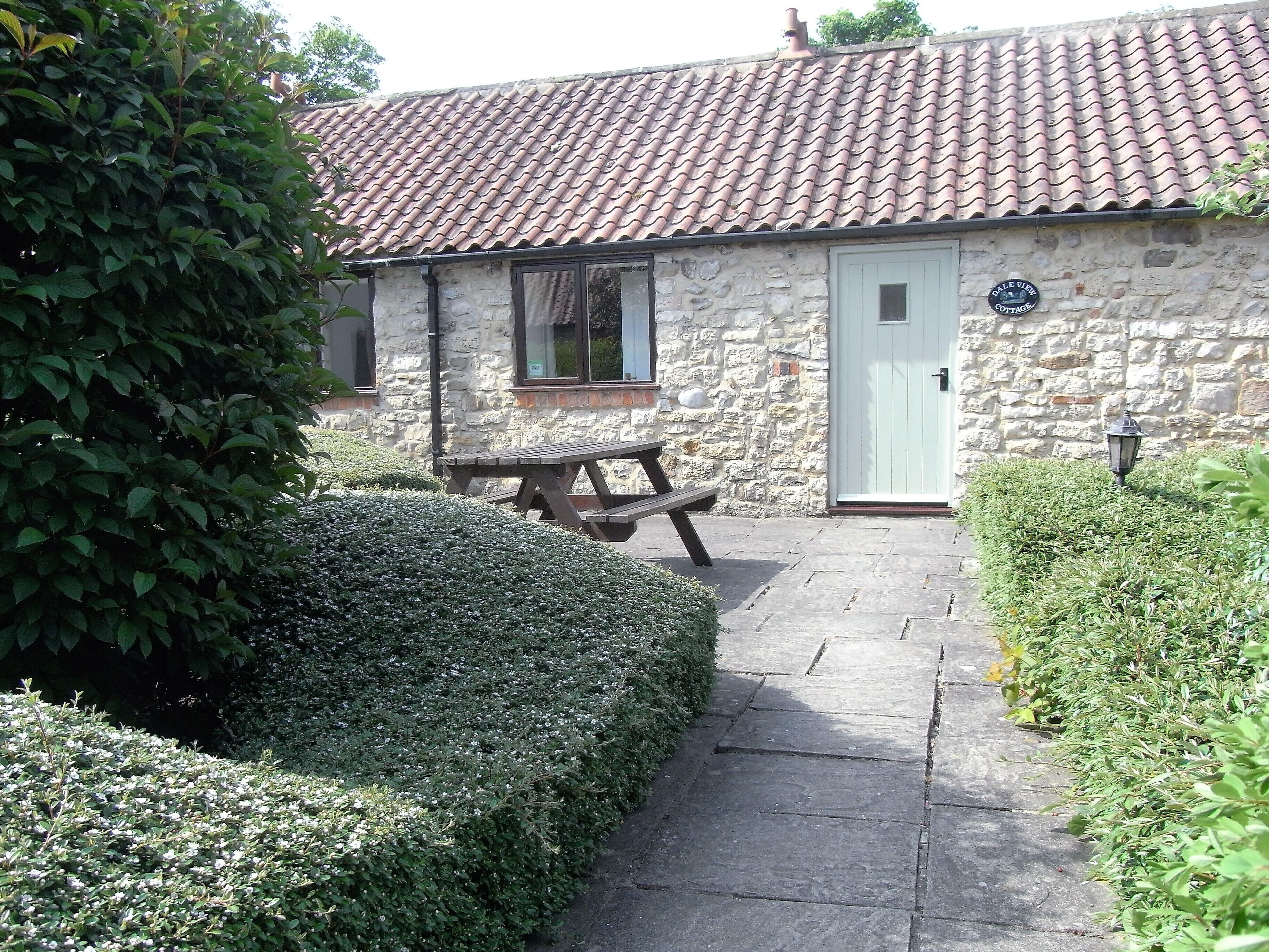 A stone cottage with a tiled roof, a wooden bench, and a well-maintained garden.