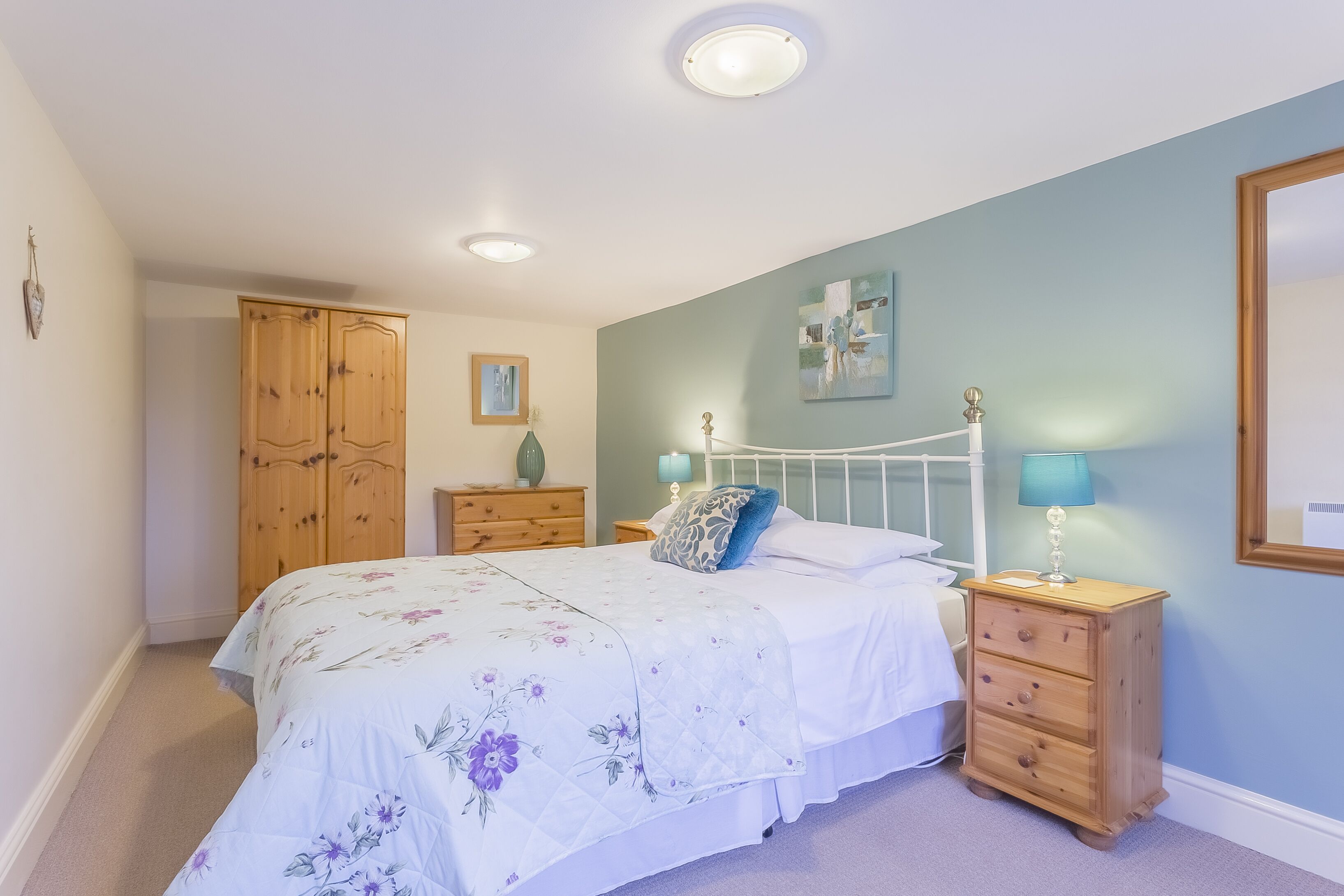 Une chambre à coucher comprenant un lit, une armoire en bois, des tables de chevet et un tableau mural.