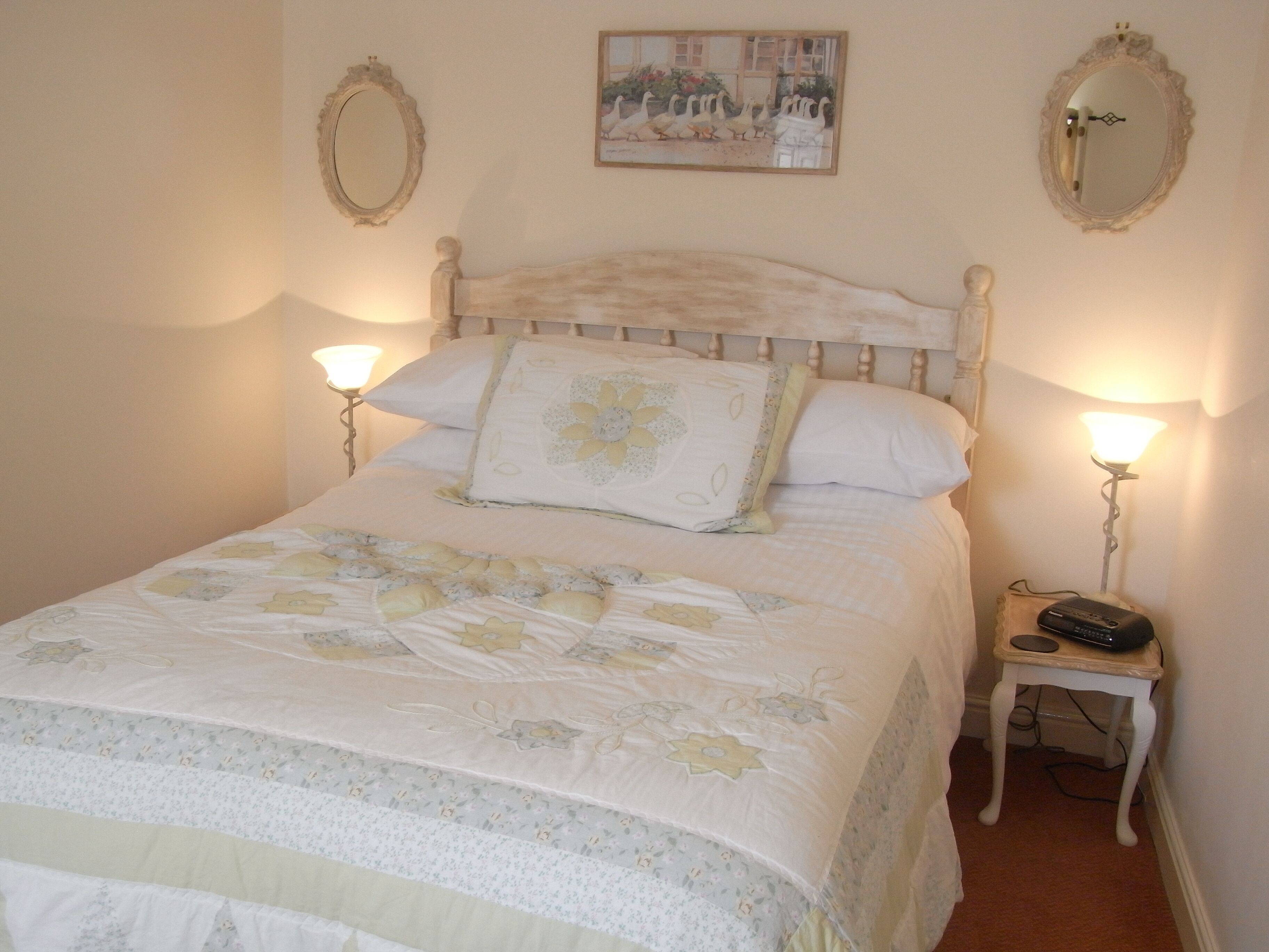 A neatly made bed with floral bedding, two bedside lamps, and a small bedside table with a remote control.