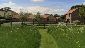 A rural setting with stone buildings, a wooden fence, and a grassy path.