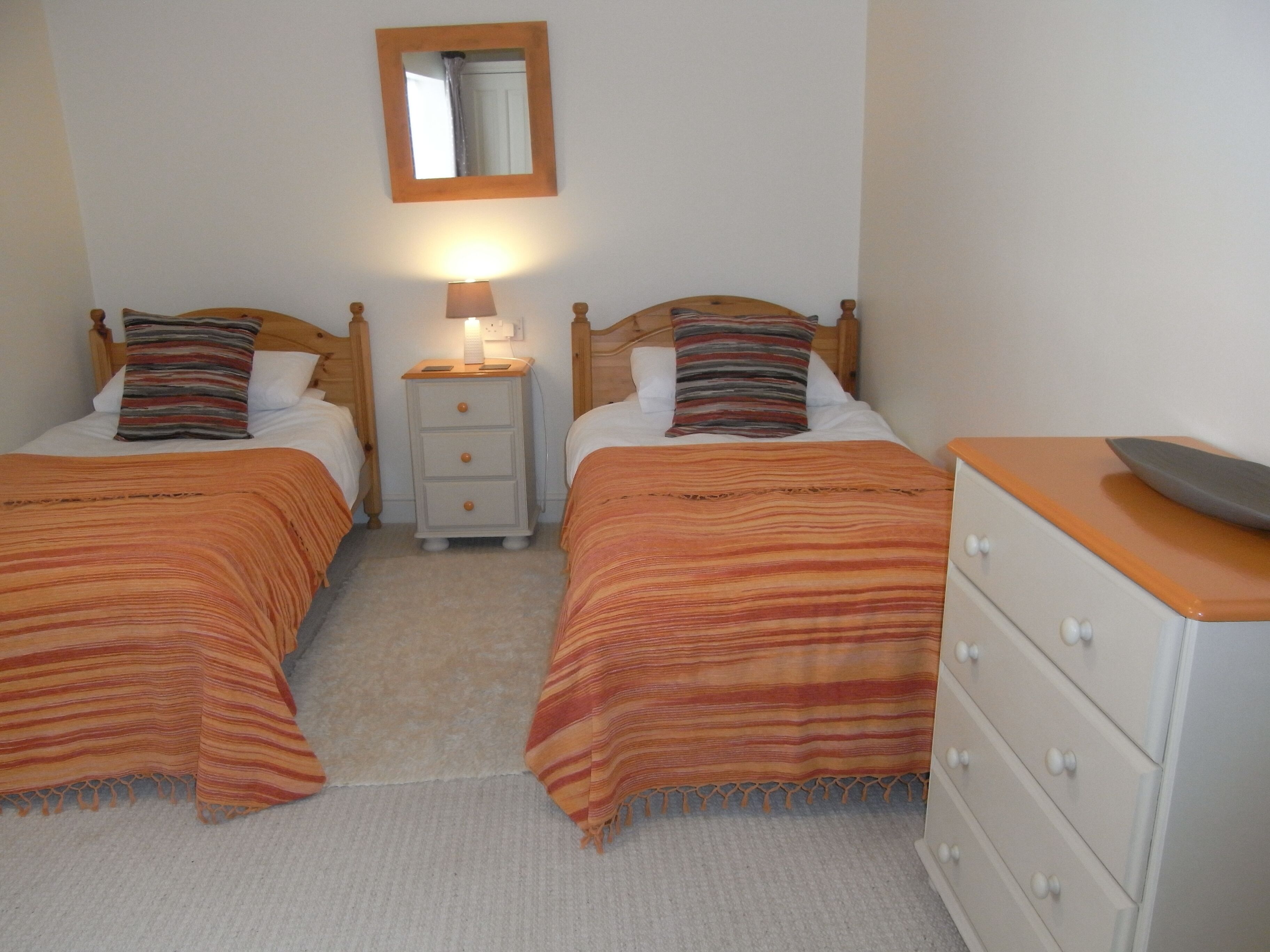 A twin room with two beds, a nightstand with a lamp, a dresser, and a mirror on the wall.