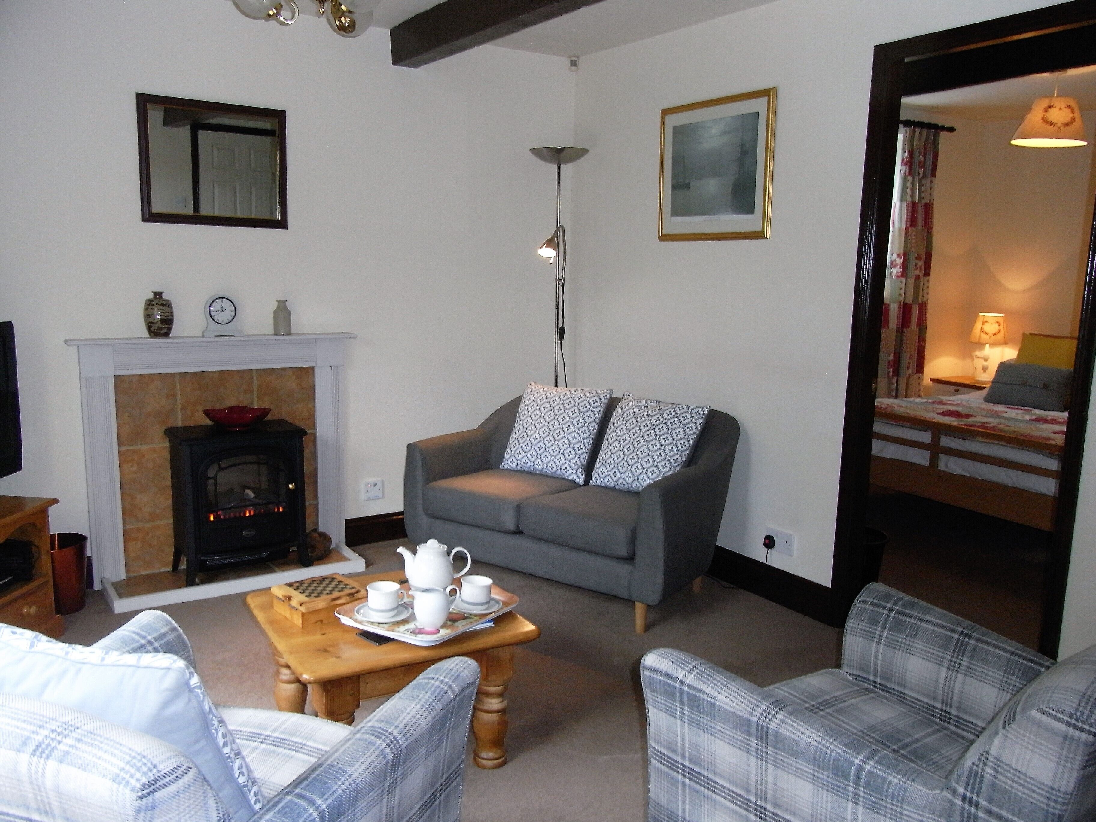 A living room with a fireplace, a sofa, a coffee table with tea set, and a bed in the adjacent room.