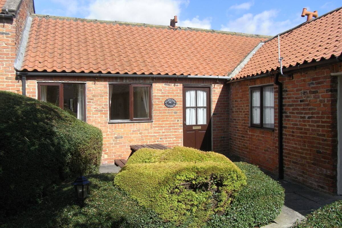 A brick cottage with a tiled roof, a small front porch, and a well-maintained hedge.