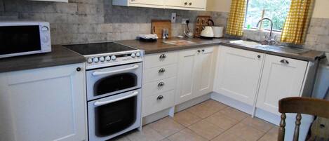 Una cocina con armarios blancos, estufa, horno, microondas, pileta y una ventana con cortinas amarillas.