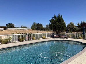A clear swimming pool with a white fence, lounge chairs, and a tree in the background. - Relaxing and Inviting Home, 2 Prime Suites, seasonally heated pool on 2.5 acre. (Atascadero)