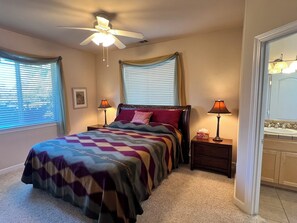 A bedroom with a bed, two bedside lamps, a ceiling fan, a window with blinds, and a bathroom visible through an open door. - Relaxing and Inviting Home, 2 Prime Suites, seasonally heated pool on 2.5 acre. (Atascadero)