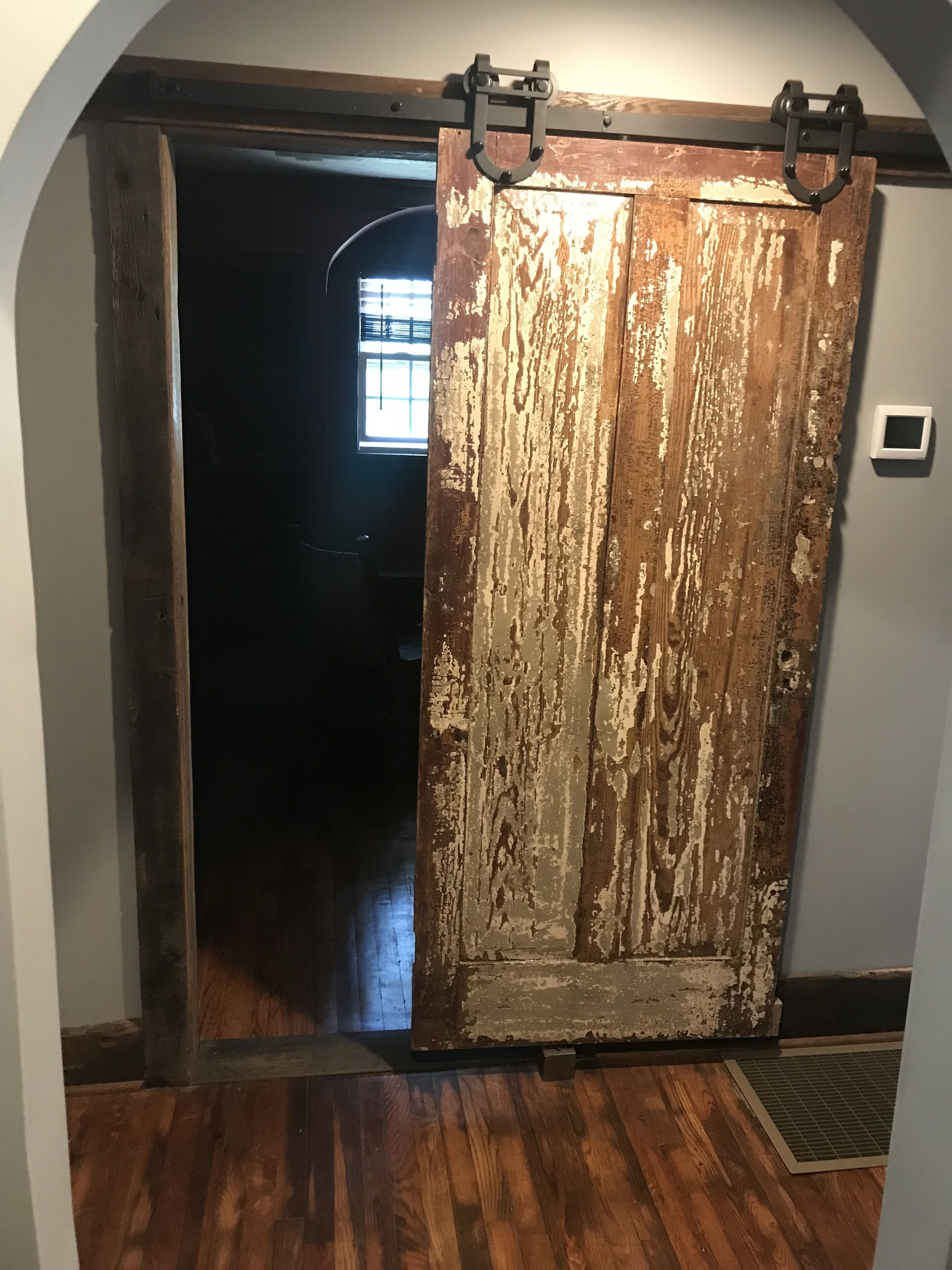 A rustic wooden door with a metal handle, leading to a dimly lit hallway.