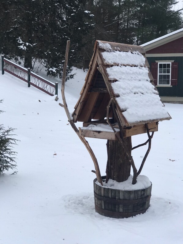 A wooden birdhouse with a slanted roof, surrounded by snow, set on a tree stump. - Sunset Ridge (Asheville)