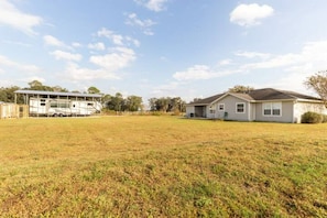 A residential property with a large open grassy yard, a detached garage, and a single-story house with a gabled roof.