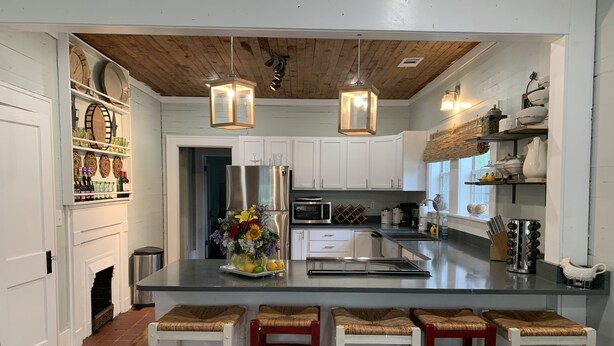 A modern kitchen with white cabinets, a stainless steel refrigerator, a central island with stools, and pendant lighting. - Rustic retreat — Car Service Available to& from Oxford, Tunica, Memphis (Sardis)