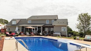 Ein Wohngebiet-Pool mit überdachter Terrasse, Gartenmöbeln und einem großen Haus im Hintergrund.