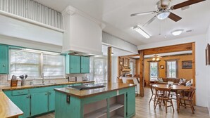 A kitchen with teal cabinets, a wooden island, and a dining area with wooden chairs and a table. - Villa 30 mins to Waco - Private Pool, Hot Tub, Gym and Fire Ring (Gatesville)
