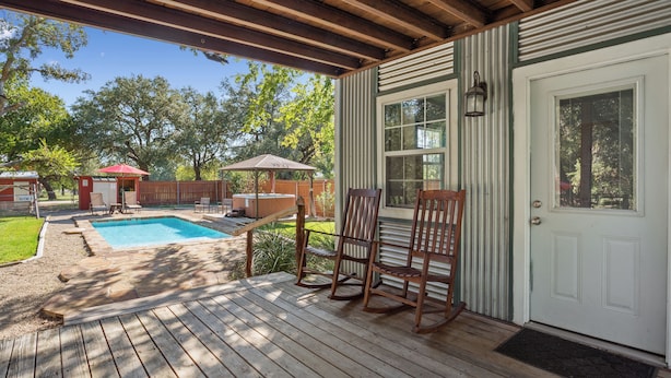 A wooden deck with a pool, rocking chairs, and a covered area with a door and windows. - Villa 30 mins to Waco - Private Pool, Hot Tub, Gym and Fire Ring (Gatesville)