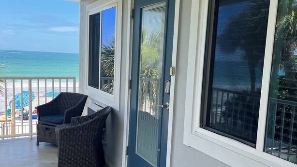 A covered porch with wicker furniture, a blue door, and large windows overlooking the ocean. - Cozy 1BR Condo w/ 0 min walk to beach! Spectacular views! Summer 2026 open! (North Redington Beach)